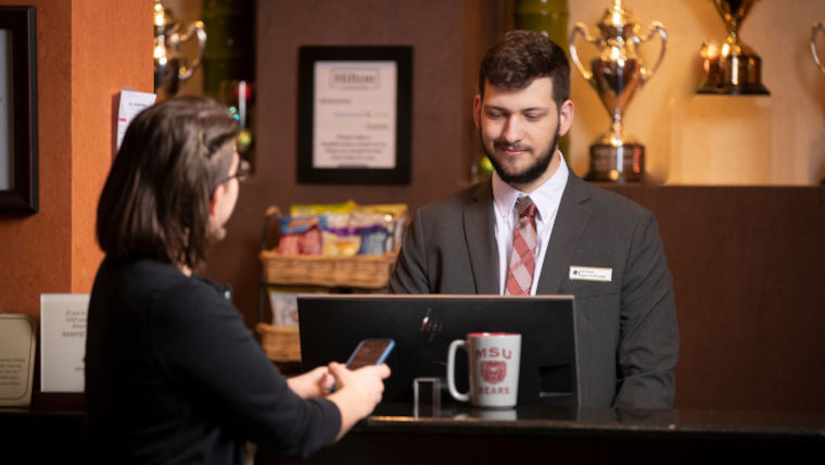 Hotel manager assisting a guest at the front desk.