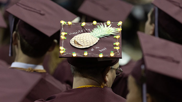 A hospitality student wears a graduation cap that reads "Hospitality at its best" during a commencement ceremony.