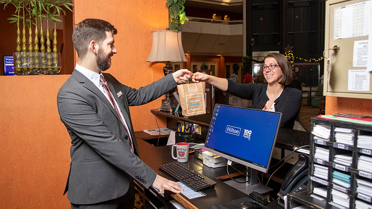 A hospitality alum hands a bag to a guest while working at the front desk of the DoubleTree hotel.