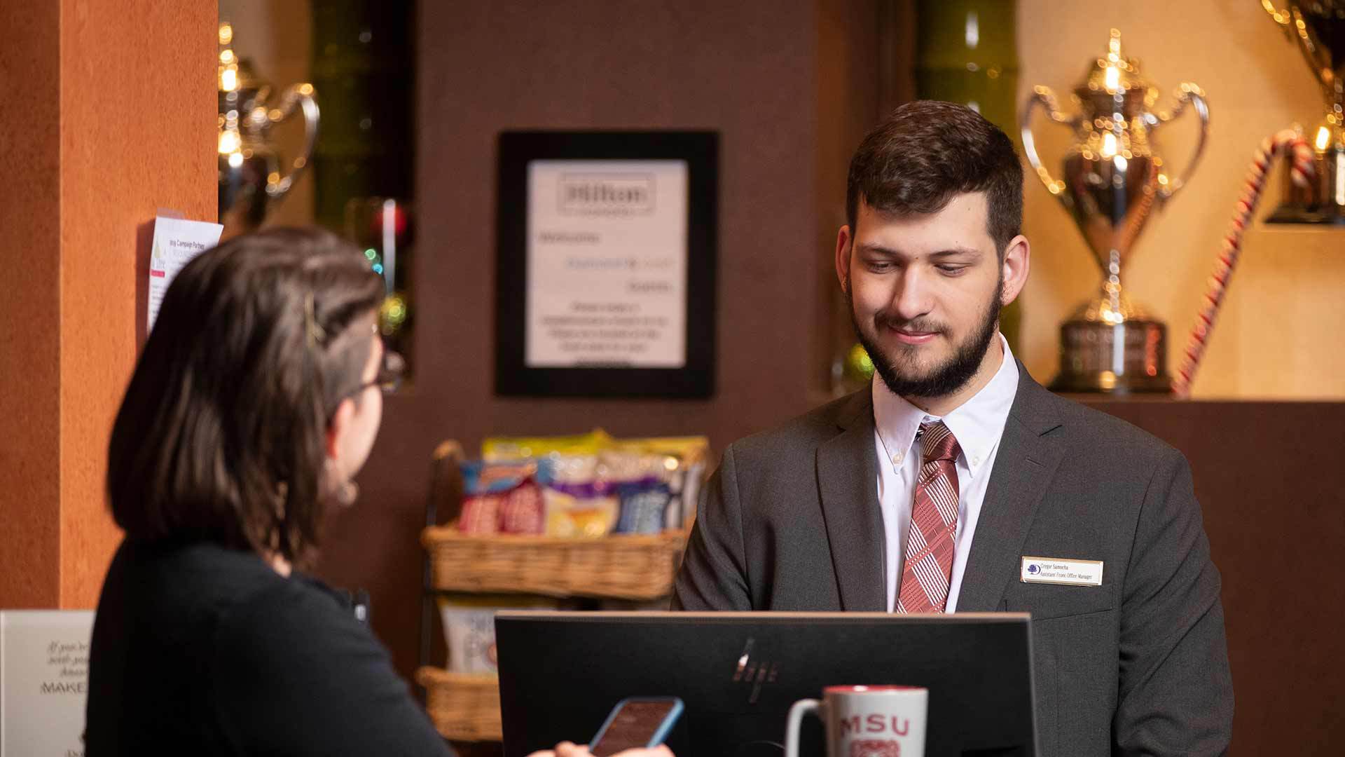 Hotel manager assisting a guest at the front desk.